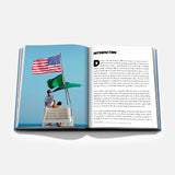 An open book, Hamptons Private by ASSOULINE, displays a photograph of two people on a lifeguard stand with American and green flags, embodying the luxury lifestyle of the Hamptons. Opposite the image, the right-hand page features introductory text—making this volume an ideal addition to any coffee table book collection.