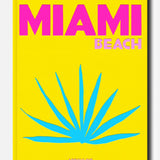 A vibrant yellow cover for ASSOULINE’s Miami Beach book features bold pink and light pink lettering, a striking blue tropical plant illustration reminiscent of the city’s iconic art deco style, and the ASSOULINE logo at the bottom.