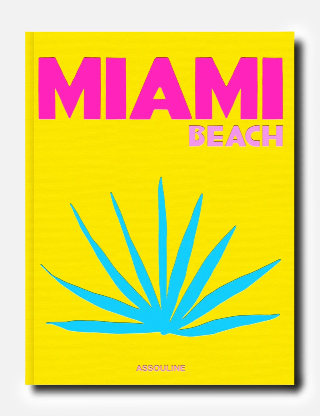 A vibrant yellow cover for ASSOULINE’s Miami Beach book features bold pink and light pink lettering, a striking blue tropical plant illustration reminiscent of the city’s iconic art deco style, and the ASSOULINE logo at the bottom.