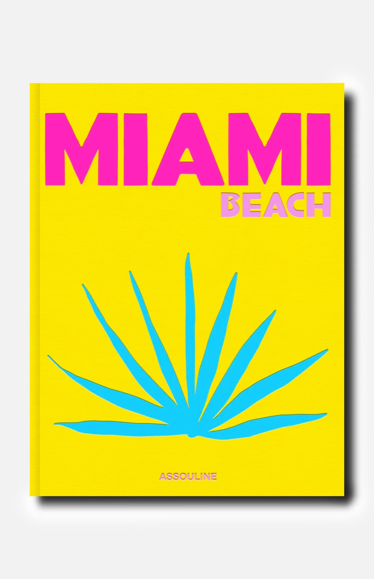 A vibrant yellow cover for ASSOULINE’s Miami Beach book features bold pink and light pink lettering, a striking blue tropical plant illustration reminiscent of the city’s iconic art deco style, and the ASSOULINE logo at the bottom.