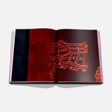 An open copy of Assouline’s "The Art of Tequila: Spirit of Mexico" book displays a red-hued, Mexican-inspired abstract artwork with intricate patterns on a white background, partially veiled in darkness on the left side.