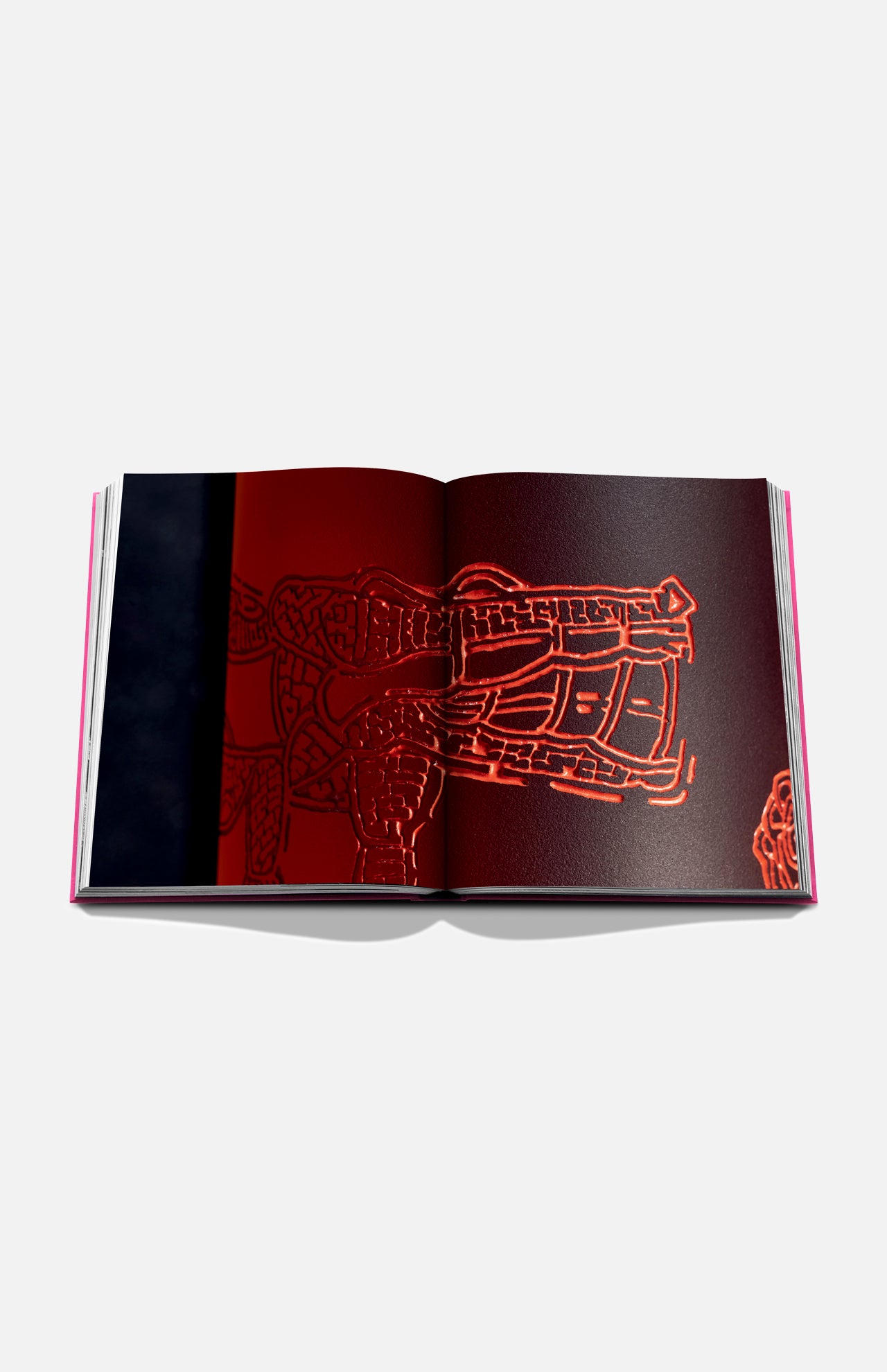 An open copy of Assouline’s "The Art of Tequila: Spirit of Mexico" book displays a red-hued, Mexican-inspired abstract artwork with intricate patterns on a white background, partially veiled in darkness on the left side.