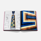 The Art of Tequila: Spirit of Mexico Book by Assouline is open, displaying geometric art in yellow, blue, black, and brown—one page features a collectible tequila bottle sketch with Greek key pattern, the other showcases colorful Mexican artwork.