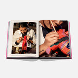 The Art of Tequila: Spirit of Mexico Book by Assouline showcases vibrant photos of Mexican art, including a person painting a decorative animal figurine. Art supplies and collectible tequila bottles are featured on the table.