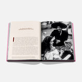The Art of Tequila: Spirit of Mexico Book by Assouline shows an open page with text and a black-and-white photo of a smiling man in a sombrero with two women, reflecting tequila history and Mexican art.