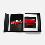 The Impossible Collection of Cars by ASSOULINE is displayed open inside its black box, featuring striking photos of classic cars—like a red vintage model—on white pages, all set against a plain white background.