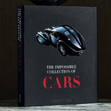 The ASSOULINE "The Impossible Collection of Cars" black coffee table book is displayed upright on a marble surface, topped with a decorative black sculpture.
