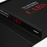 A black hardcover copy of ASSOULINE’s The Impossible Collection of Cars lies partly inside an open matching black box, with the brand name visible on its spine.