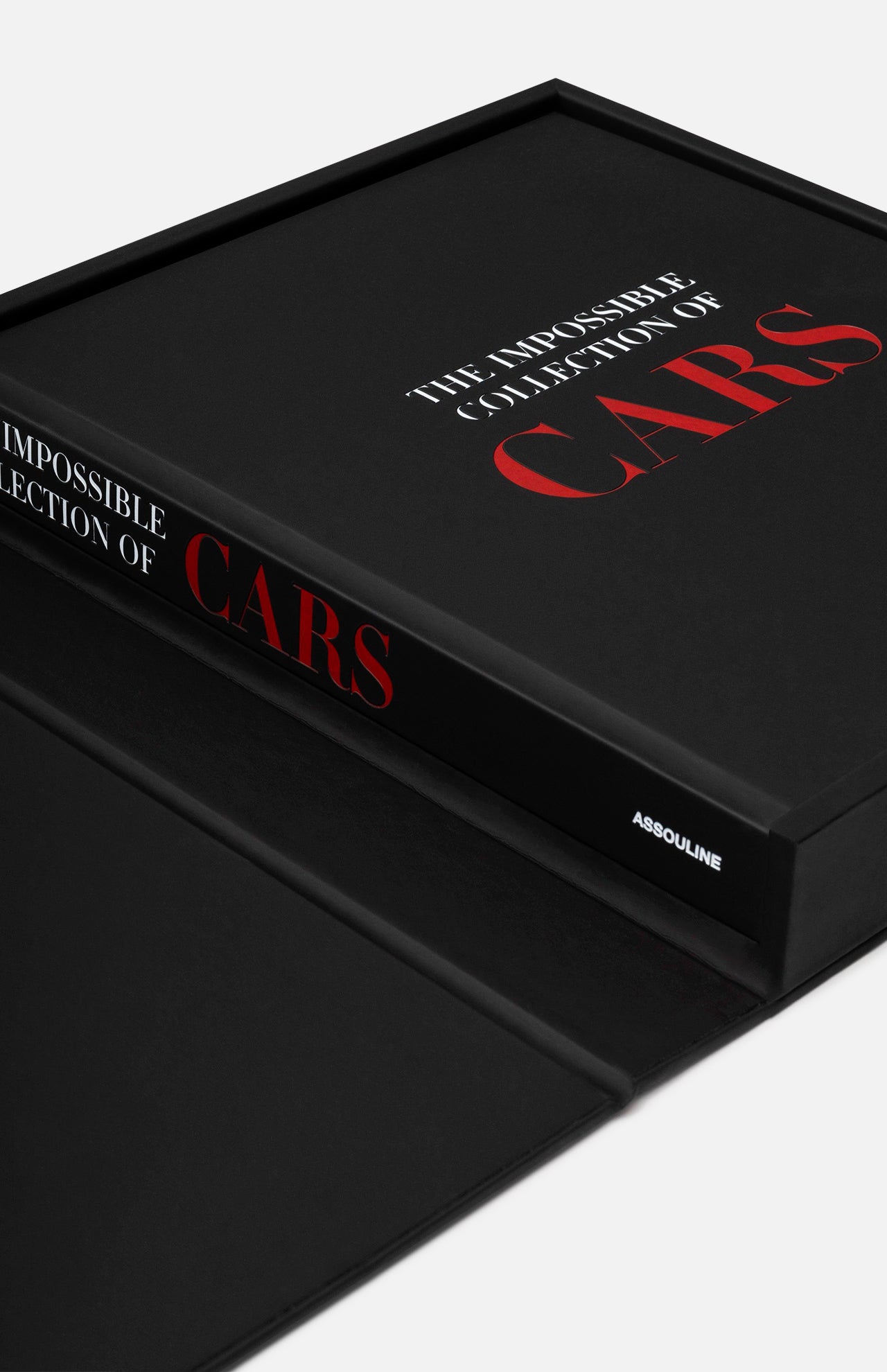 A black hardcover copy of ASSOULINE’s The Impossible Collection of Cars lies partly inside an open matching black box, with the brand name visible on its spine.