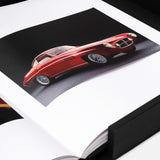 An open book from ASSOULINE’s "The Impossible Collection of Cars" displays a striking vintage red sports car photo on a black background, housed in a black presentation box—honoring the world’s most exceptional automobiles.