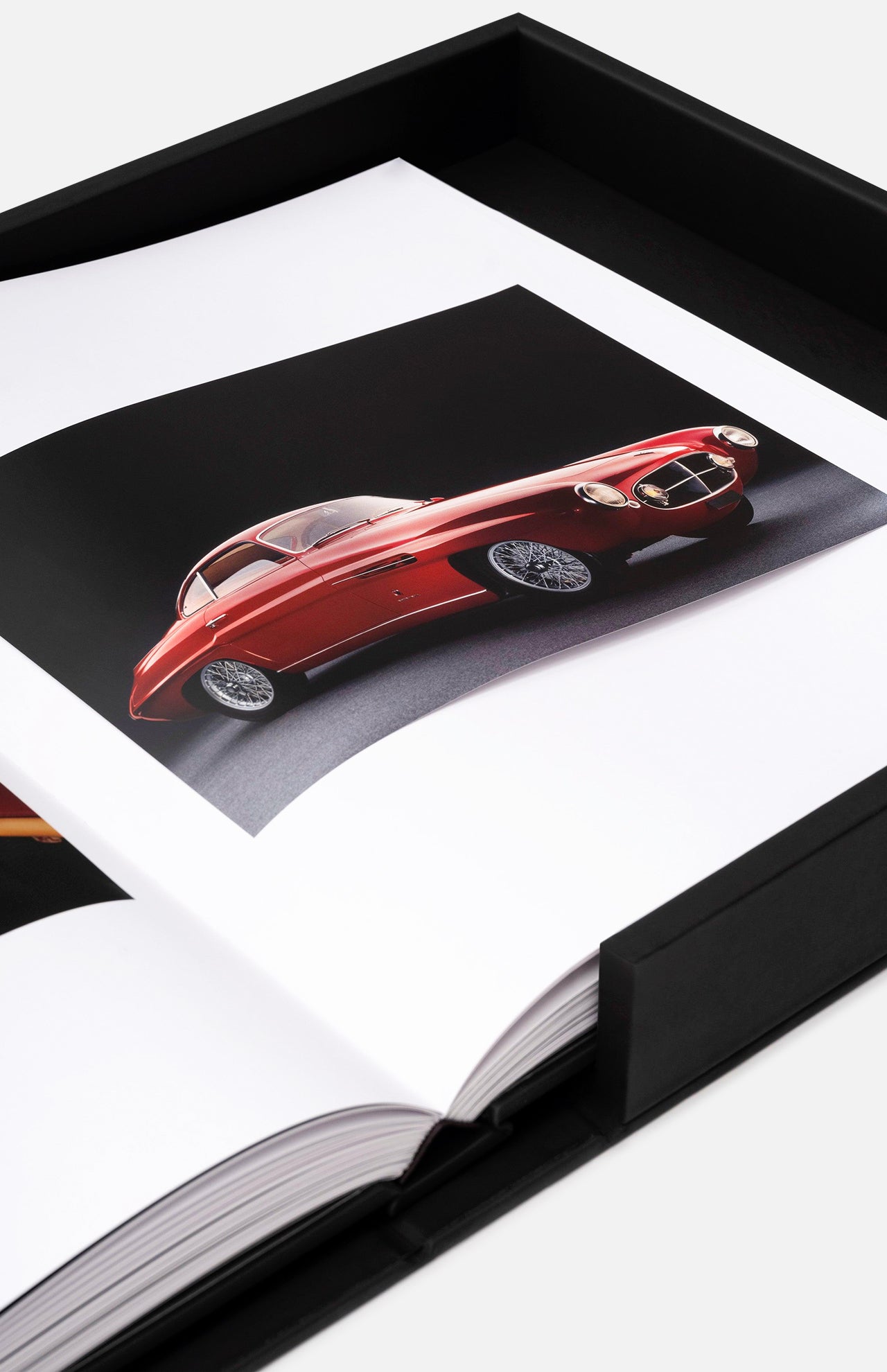 An open book from ASSOULINE’s "The Impossible Collection of Cars" displays a striking vintage red sports car photo on a black background, housed in a black presentation box—honoring the world’s most exceptional automobiles.