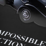 Close-up of a glossy black vintage luxury car on a dark background, positioned above partially visible white and red text reading "The Impossible Collection of Cars" by ASSOULINE.