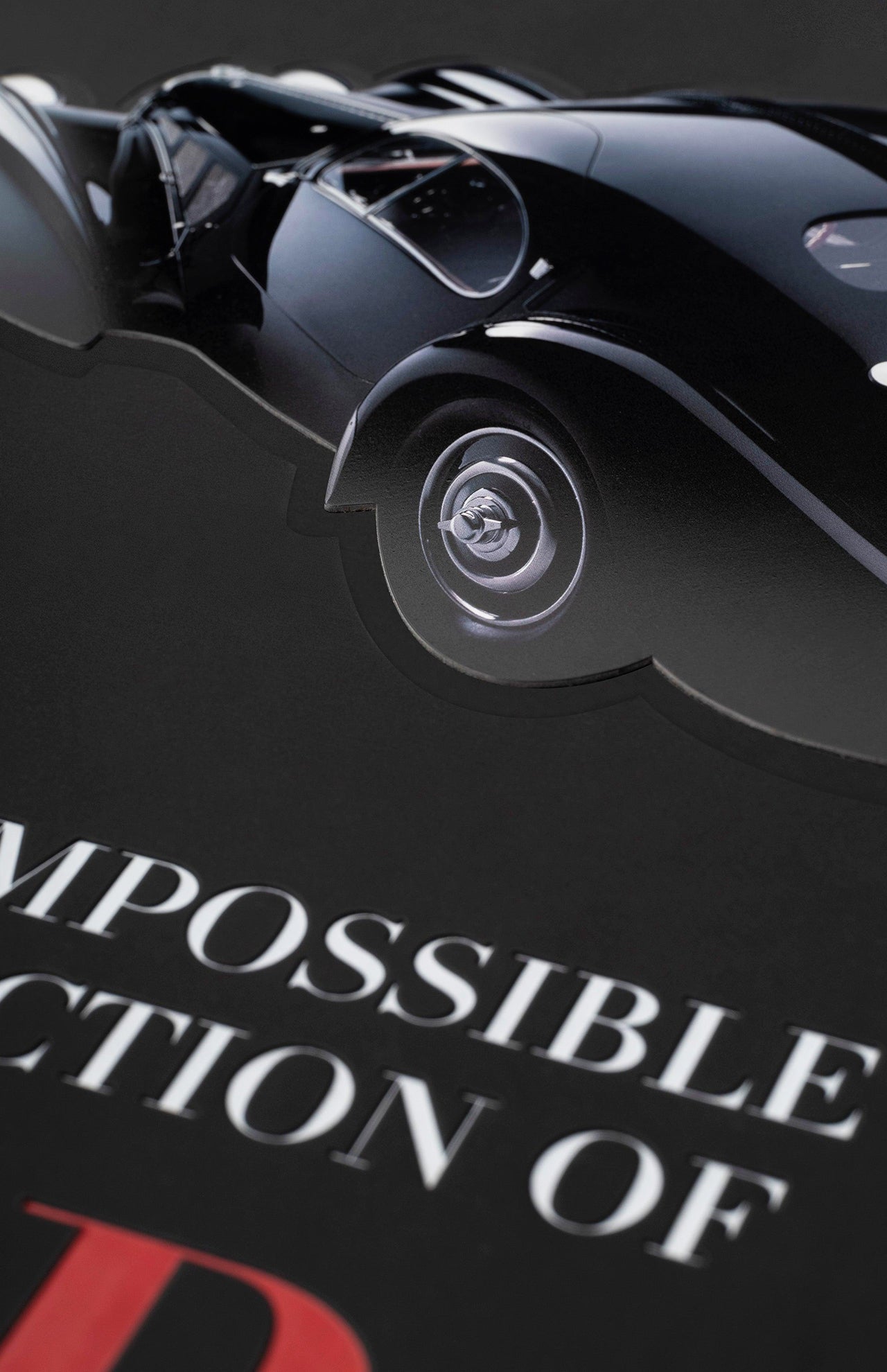 Close-up of a glossy black vintage luxury car on a dark background, positioned above partially visible white and red text reading "The Impossible Collection of Cars" by ASSOULINE.