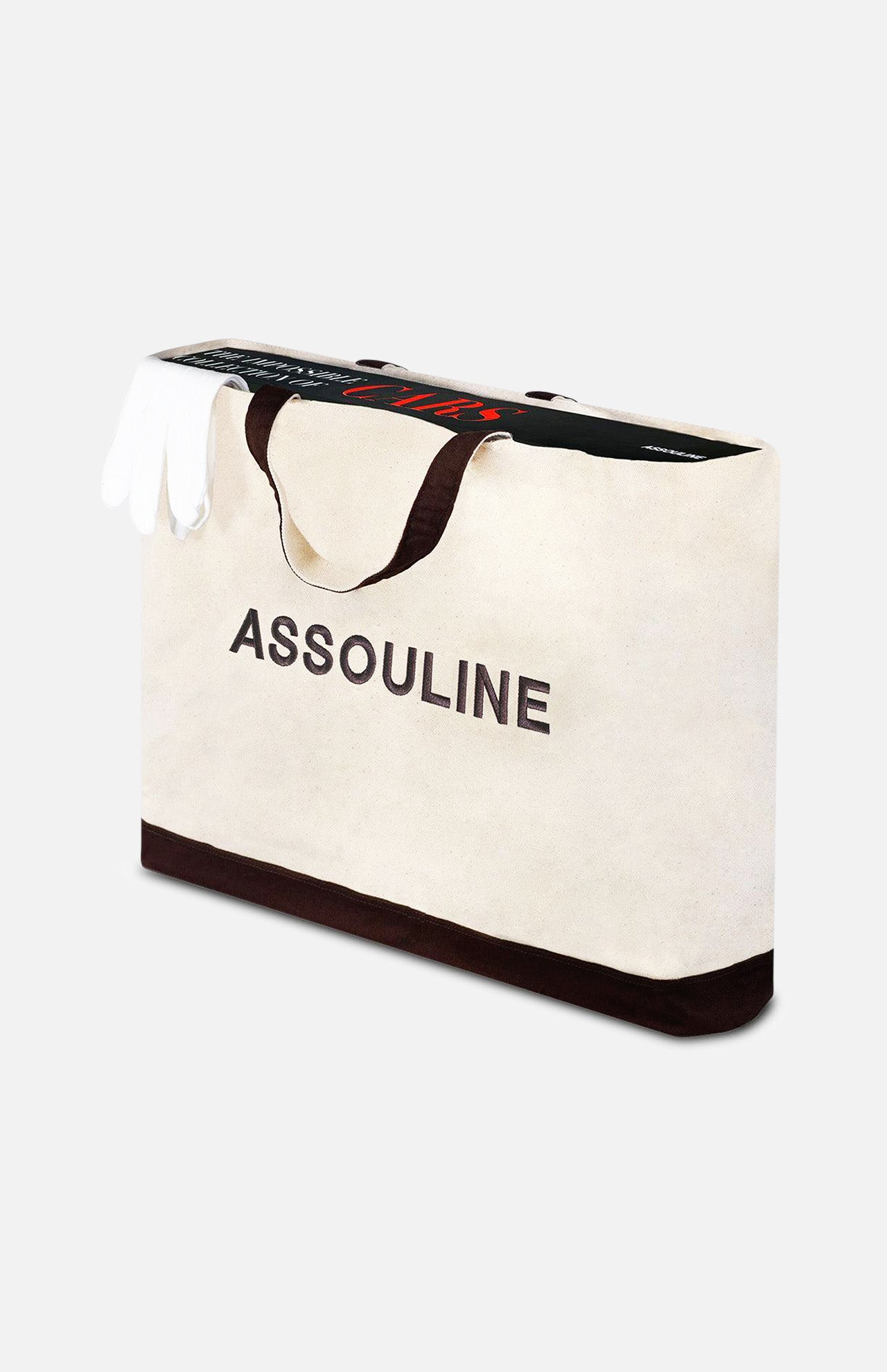 A large white ASSOULINE canvas tote with black handles and trim holds a pair of white gloves and "The Impossible Collection of Cars" book by ASSOULINE, both partially visible inside the bag.
