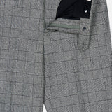 The Peak Lapel Plaid Suit by ATELIER MUNRO features gray plaid wool fabric with a subtle black and white check, partially unzipped to display the waistband, button, and zipper details.