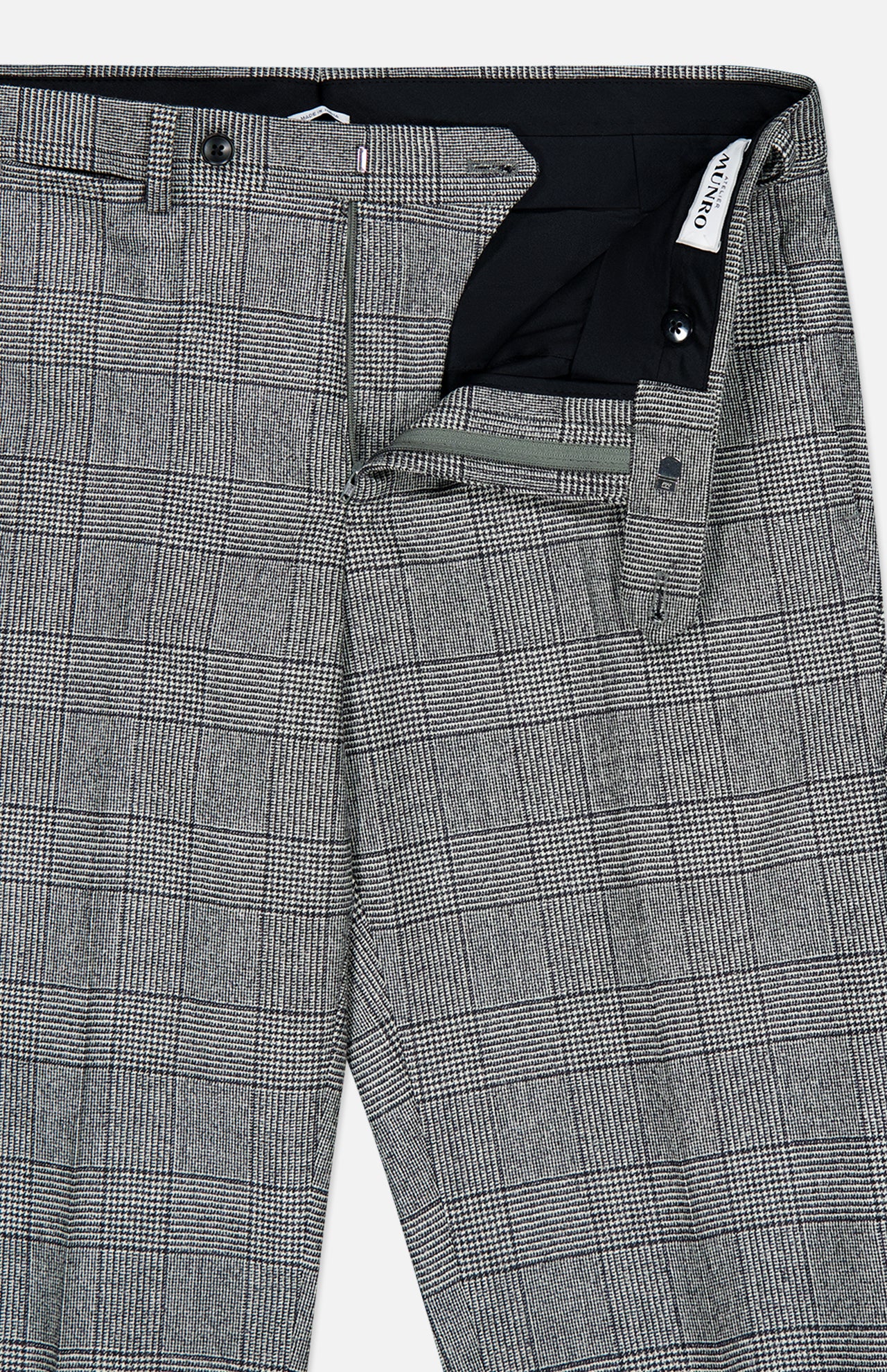 The Peak Lapel Plaid Suit by ATELIER MUNRO features gray plaid wool fabric with a subtle black and white check, partially unzipped to display the waistband, button, and zipper details.