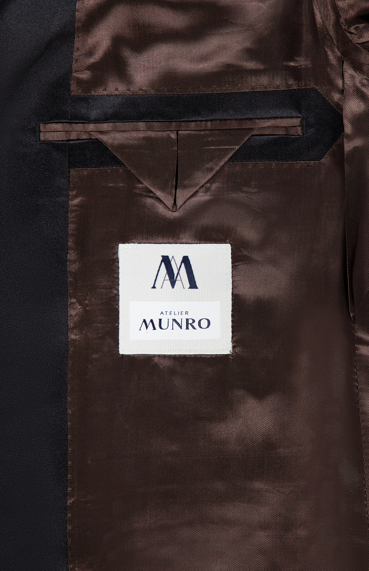 Close-up of the Shawl Lapel Tuxedo Suit’s dark brown lining with an interior pocket and a white ATELIER MUNRO label in blue and black text.