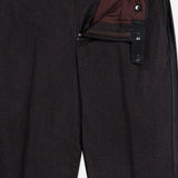 ATELIER MUNRO’s Shawl Lapel Tuxedo Suit features dark formal trousers with a partially open zipper, unbuttoned waistband with black adjusters, burgundy lining, and subtly textured pure wool fabric.
