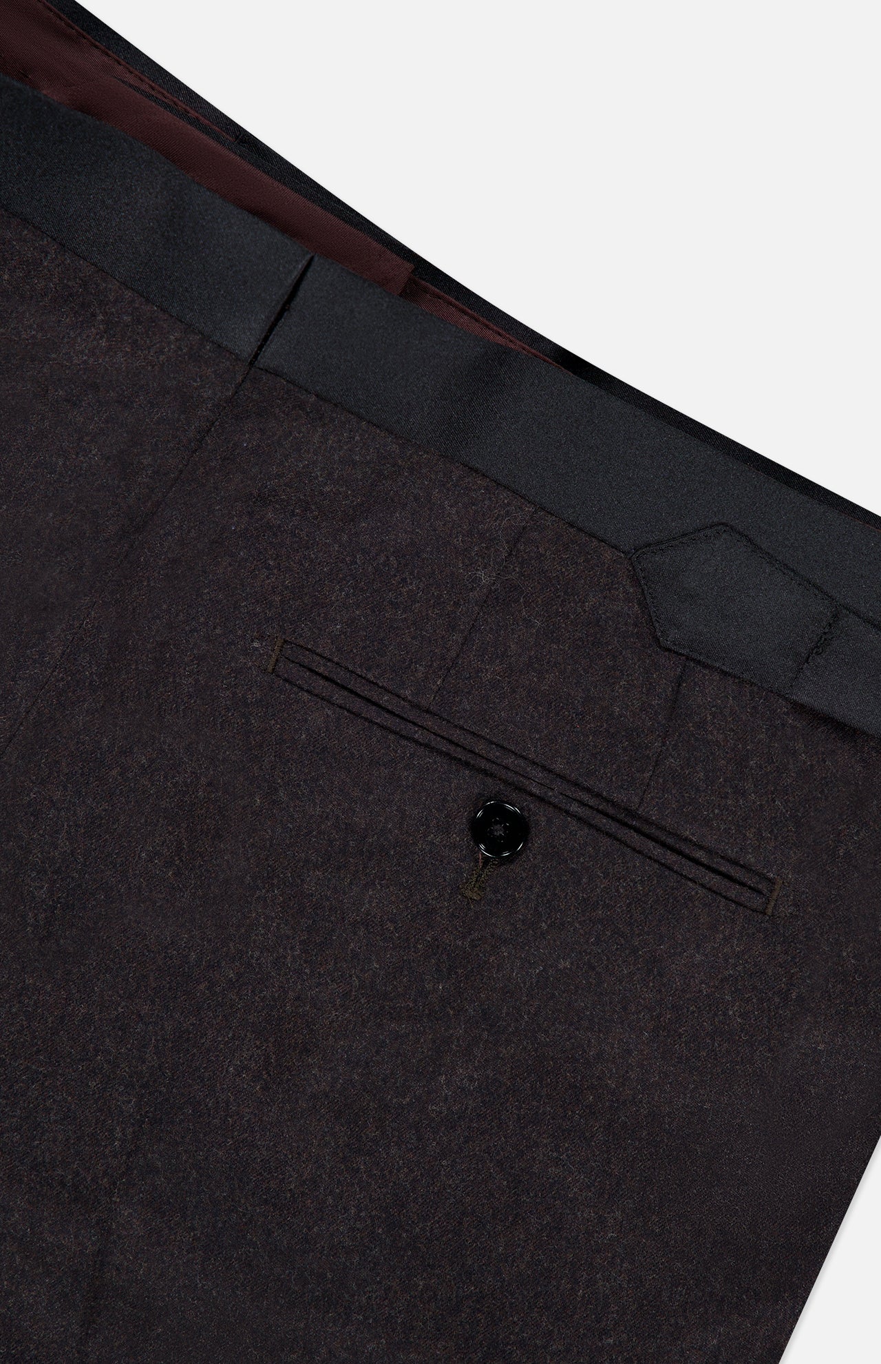 Close-up of the back pocket on dark dress pants from the Shawl Lapel Tuxedo Suit by ATELIER MUNRO, featuring a single-button closure and black waistband detail against a light background.