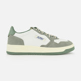 The AUTRY Medalist Low Leather Suede Sneaker features a white and gray design with green accents, cream laces, and a green sole. Inspired by 1980s tennis shoes, it sports the AUTRY logo and an American flag on the side for a classic retro look.
