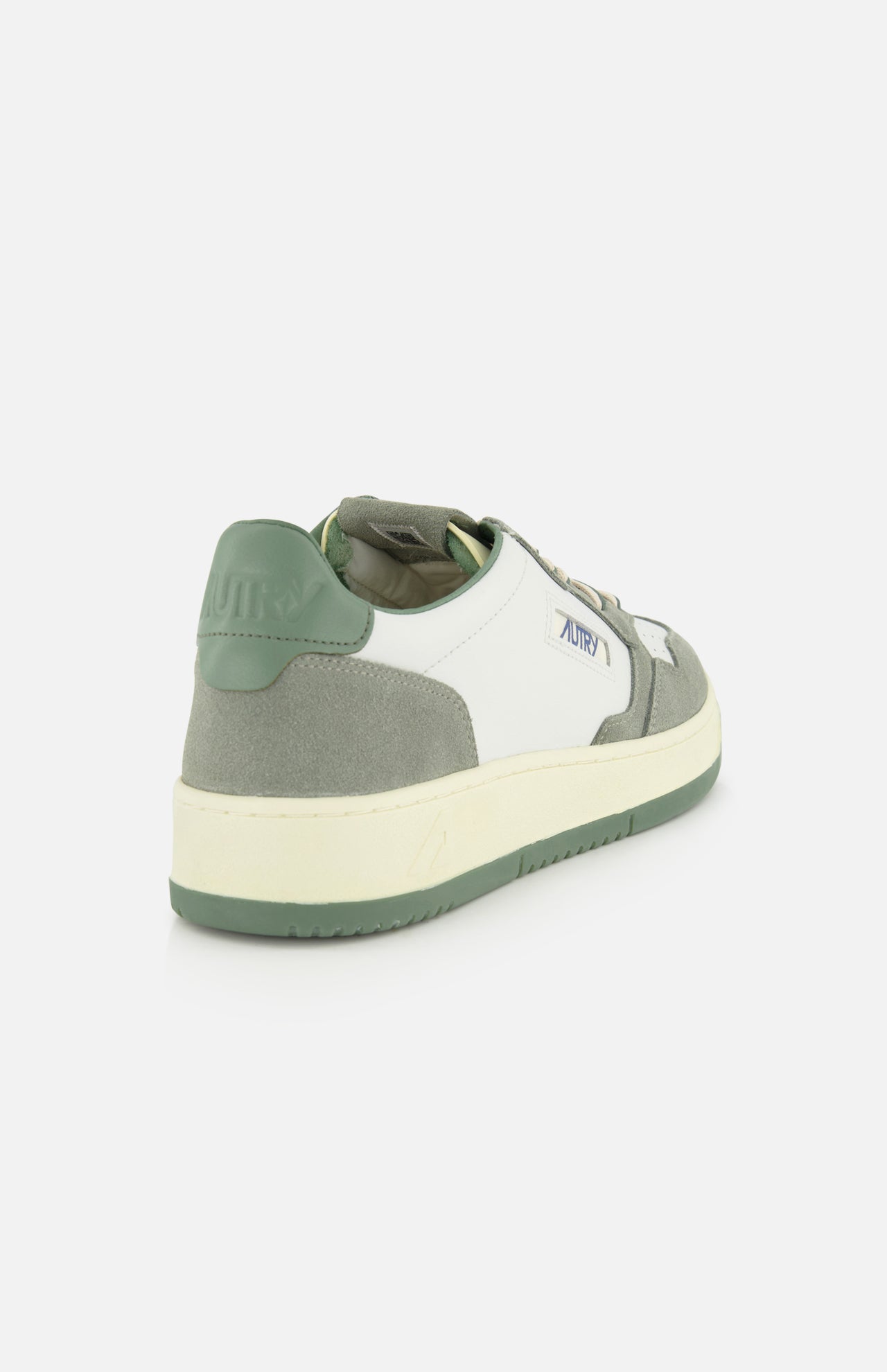 The AUTRY Medalist Low Leather Suede Sneaker is a stylish white 1980s-inspired tennis shoe with green suede accents, platform sole, green heel tab, and Autry branding on the side and heel, shown from a rear diagonal angle on a white background.