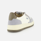 The AUTRY Medalist Low Man Leather Suede Sneaker is displayed from a rear side angle on a plain white background, showcasing its stylish combination of white, light gray, and beige hues. Inspired by classic 1980s tennis shoes, this sneaker features a suede heel detail, platform sole, rubber outsole, and a distinctive branded patch on the side.