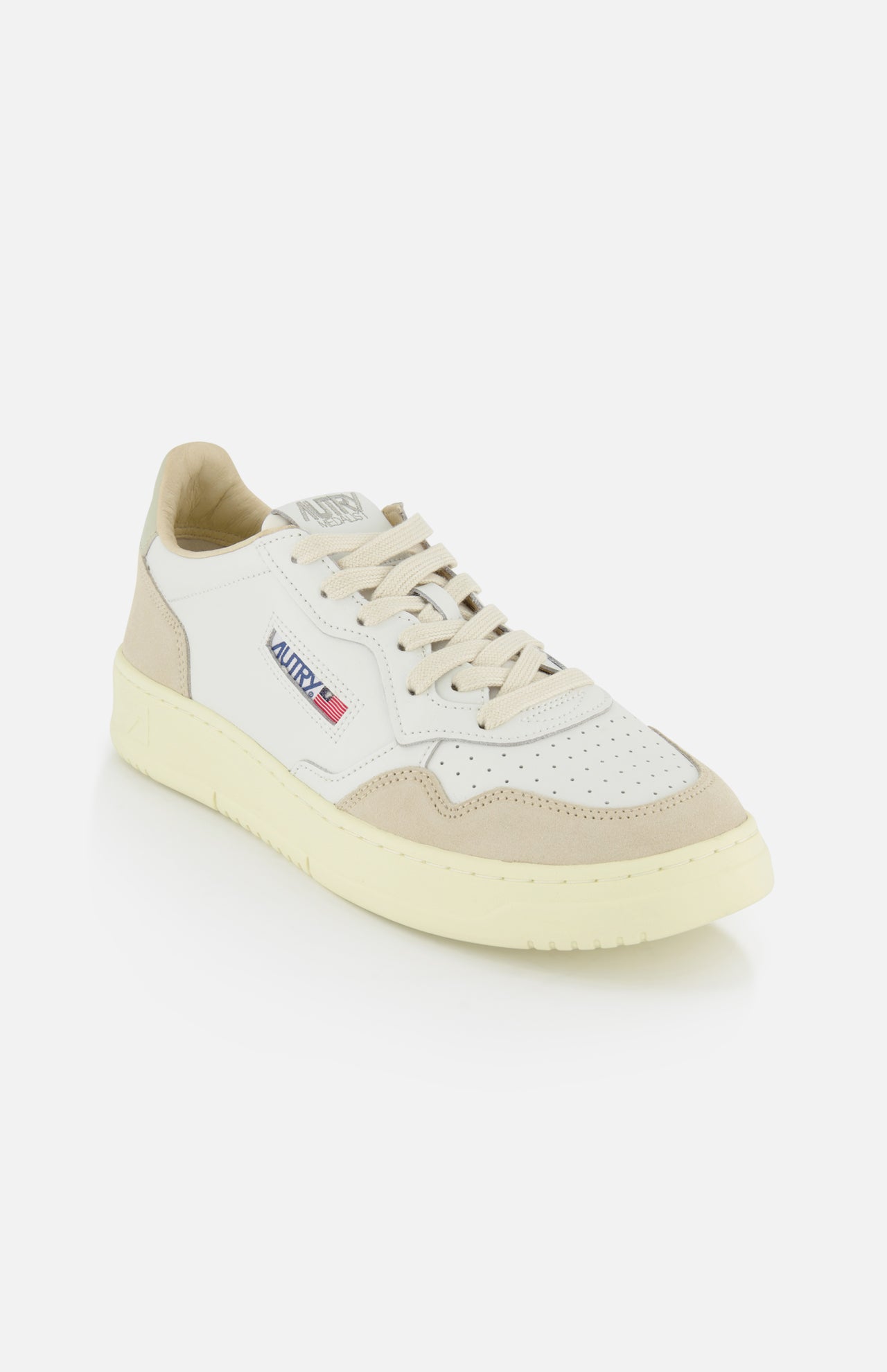 The AUTRY Medalist Low Man Leather Suede Sneaker features a white and beige leather-suede upper, perforated details, cream sole and laces, plus a side patch displaying “AUTRY” and an American flag. Shown on a plain white background.
