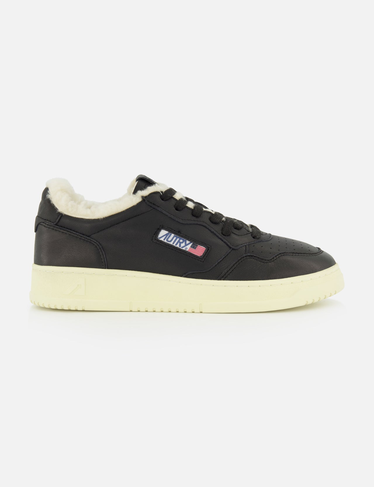 The Medalist Low Man Shearling Sneaker by AUTRY is a black low-top leather sneaker featuring a cream platform sole, plush shearling lining, and a small AURA logo patch with red, white, and blue stripes on the side. The shoe is shown against a plain white background.
