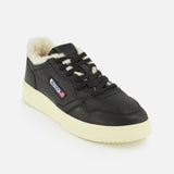 The AUTRY Medalist Low Man Shearling Sneaker features black leather uppers, a cream rubber sole, matching black laces, and a warm shearling lining. A side patch displays the brand’s flag design and logo. The shoe is presented against a white background.
