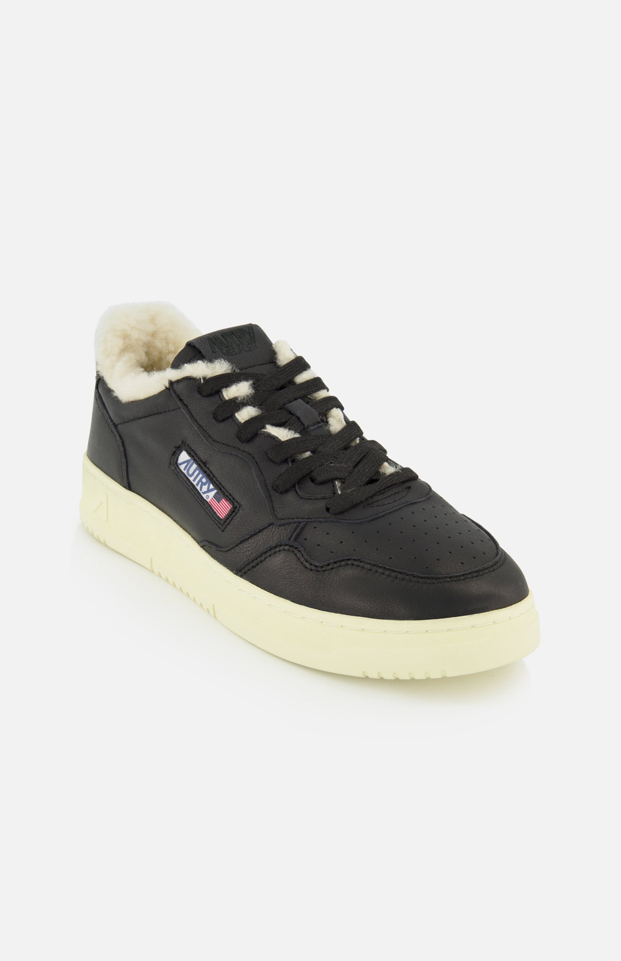 The AUTRY Medalist Low Man Shearling Sneaker features black leather uppers, a cream rubber sole, matching black laces, and a warm shearling lining. A side patch displays the brand’s flag design and logo. The shoe is presented against a white background.