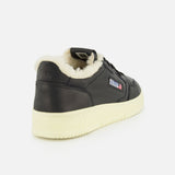 The AUTRY Medalist Low Man Shearling Sneaker, featuring black leather, an off-white platform sole, and a plush cream-colored shearling lining, is displayed from the back-left angle against a plain white background.