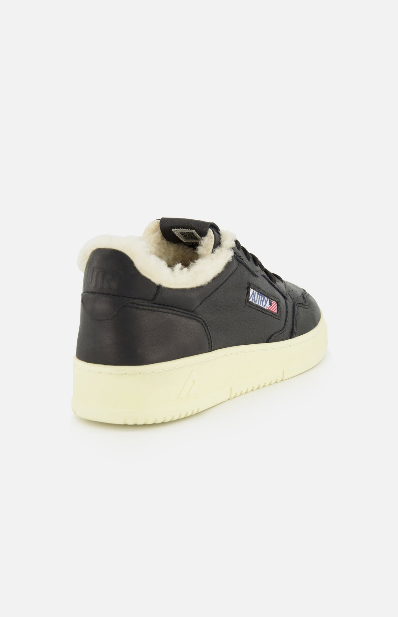 The AUTRY Medalist Low Man Shearling Sneaker, featuring black leather, an off-white platform sole, and a plush cream-colored shearling lining, is displayed from the back-left angle against a plain white background.