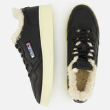 Two black Medalist Low Man Shearling Sneakers by AUTRY, featuring cream-colored platform soles and a plush white shearling lining. One shoe is seen from the side and the other from above, showcasing the AUTRY logo and an American flag patch.