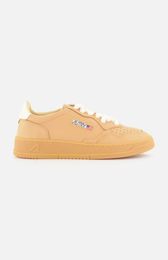 The AUTRY Medalist Low Man Sneaker features tan leather, a light brown sole, white knit laces, an embroidered American flag and "AUTRY" patch on the side, and a white heel, shown in profile against a white background.