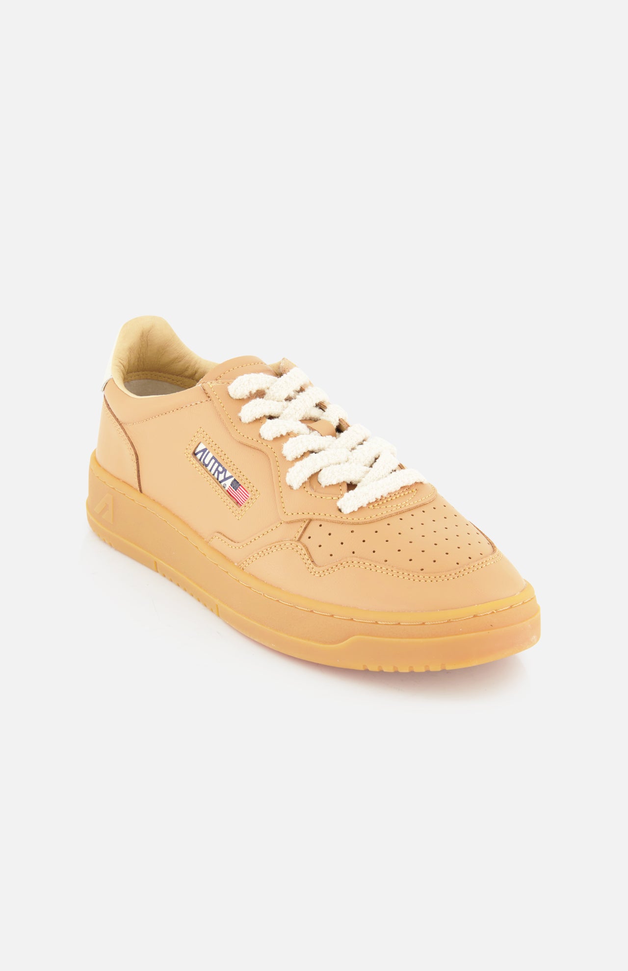 The AUTRY Medalist Low Man Sneaker features a tan leather upper, white knit laces, a gum rubber sole, and a small rectangular side patch displaying the AUTRY brand name and American flag. Photographed on a white background.