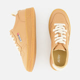 The AUTRY Medalist Low Man Sneaker features tan leather, chunky knit white laces, gum soles, and a low-top silhouette. Shown from side and top views, one shoe displays the AUTRY logo patch with an American flag on the side.