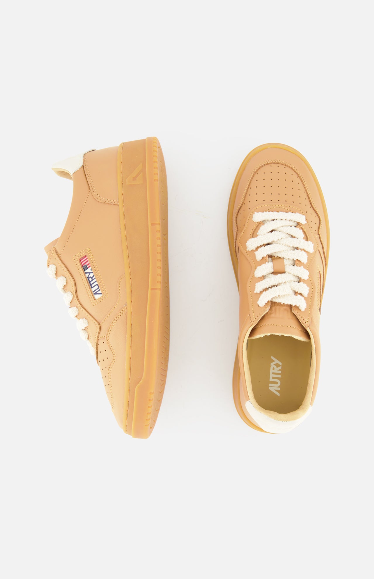 The AUTRY Medalist Low Man Sneaker features tan leather, chunky knit white laces, gum soles, and a low-top silhouette. Shown from side and top views, one shoe displays the AUTRY logo patch with an American flag on the side.