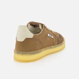 The AUTRY Medalist Low Man Suede Leather Sneaker, featuring a brown suede upper, white laces, a white heel tab, and a translucent yellow sole, is displayed at an angle on a white background.