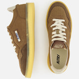 A pair of AUTRY Medalist Low Man Suede Leather Sneakers in brown suede, inspired by vintage tennis shoes and featuring yellow soles, white laces, and signature side branding, displayed from both side and top views against a white background.