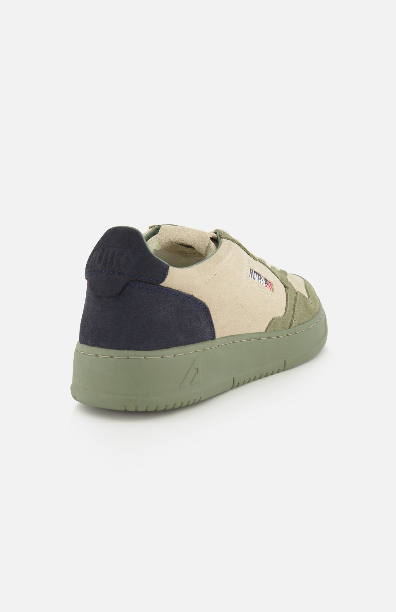 The AUTRY Medalist Low Man Suede Sneaker is a low-top shoe in beige and olive green multicolored suede, accented with a dark navy heel, green platform sole, and subtle side logo details. It’s presented from a rear-angled view against a white background.