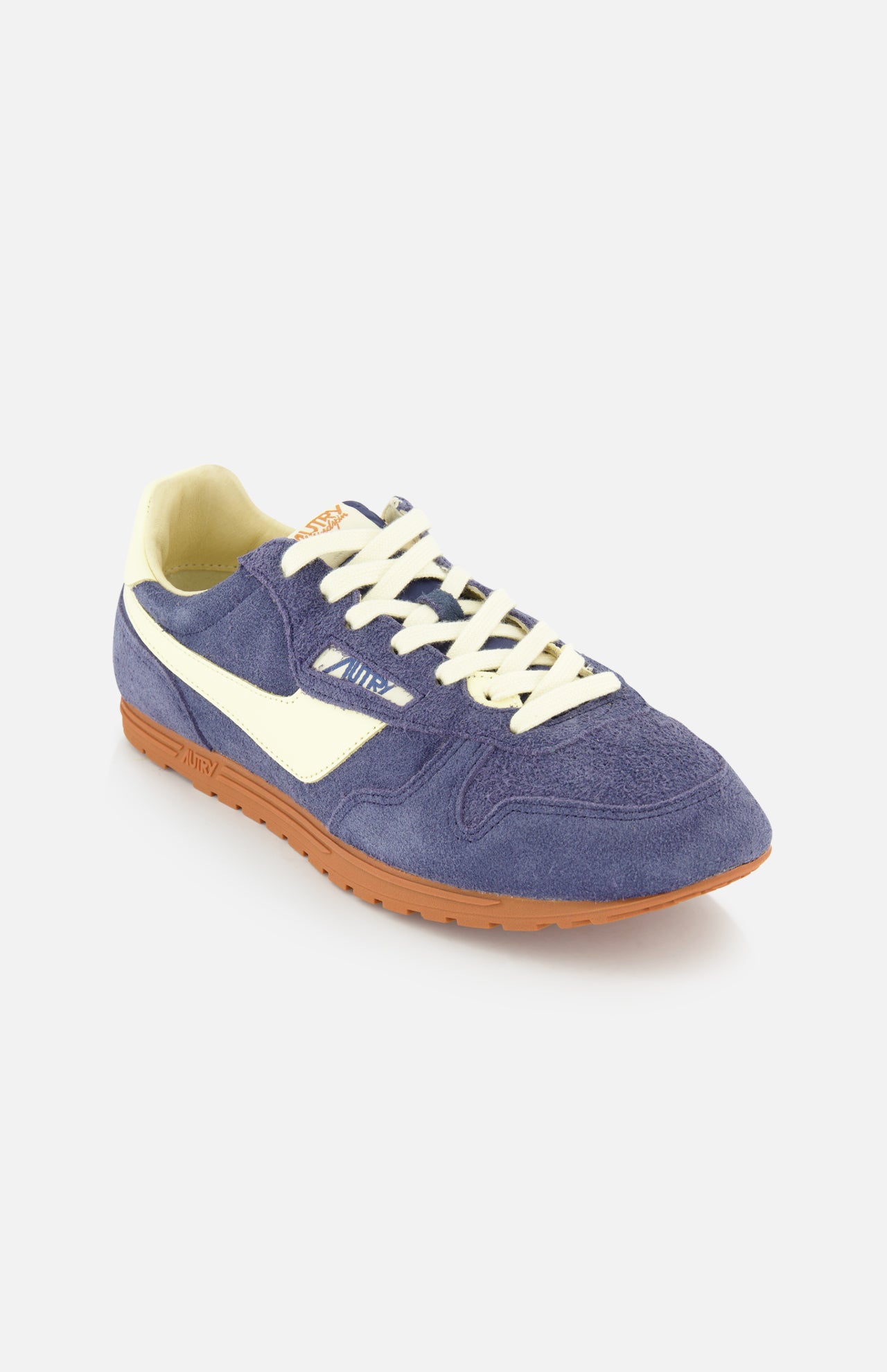 The AUTRY Windspin Low Suede Sneaker features purple suede, white laces and side stripe, a beige lining, and a brown rubber sole for retro 60s style—all set against a crisp white background.