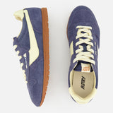 The AUTRY Windspin Low Suede Sneaker features blue suede uppers, off-white accents, and brown rubber soles. One 60s-inspired sneaker appears side-on; the other is shown from above against a plain white background.