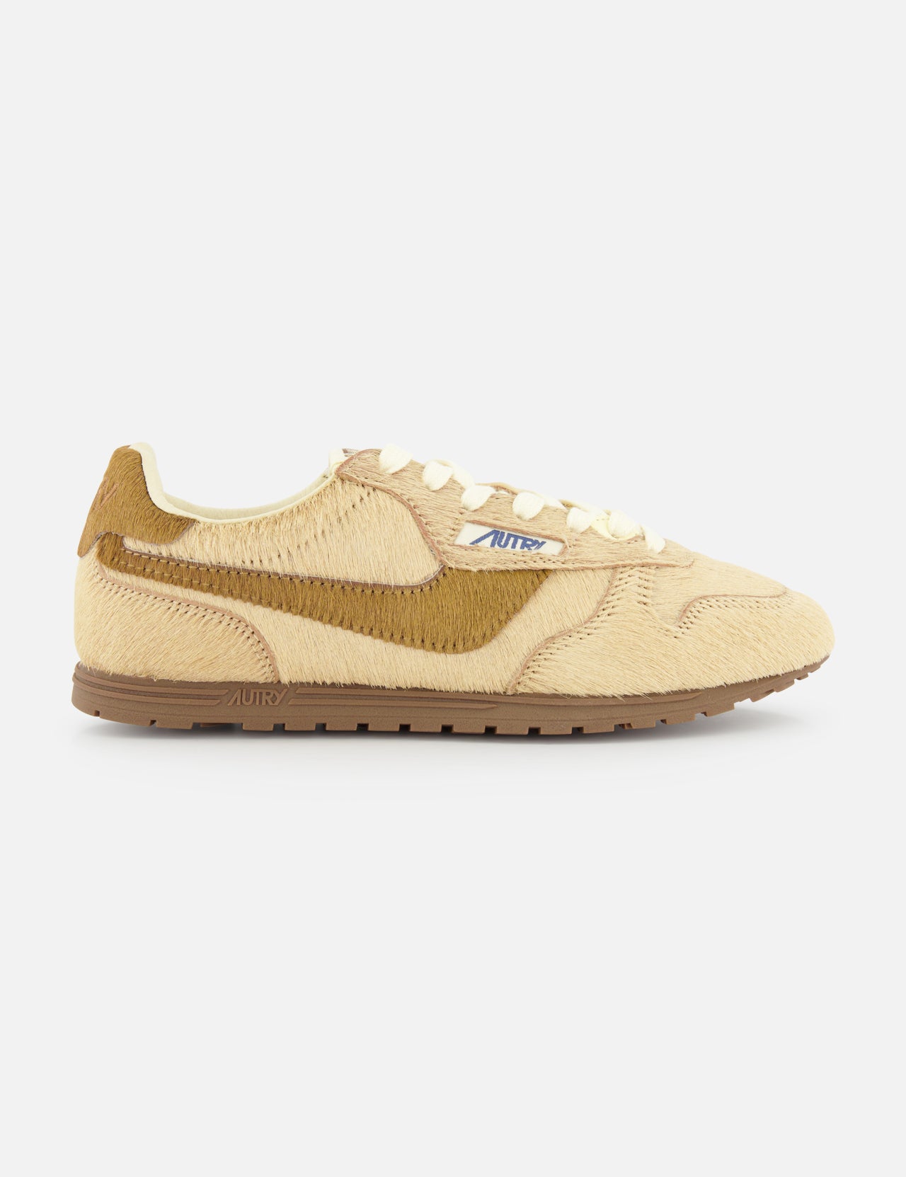 The AUTRY Windspin Low Faux Pony Hair Sneaker features a beige, hair-like textured upper, cream laces, brown swoosh detail, and an ultra-flat rubber sole, displayed on a plain white background.