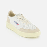 The AUTRY Medalist Low Gold Heel Sneaker features a white leather upper with beige accents, a perforated toe, cream platform sole, and the AUTRY logo with a small American flag on the side, capturing the vintage style of 1980s tennis shoes. It is displayed against a plain white background.