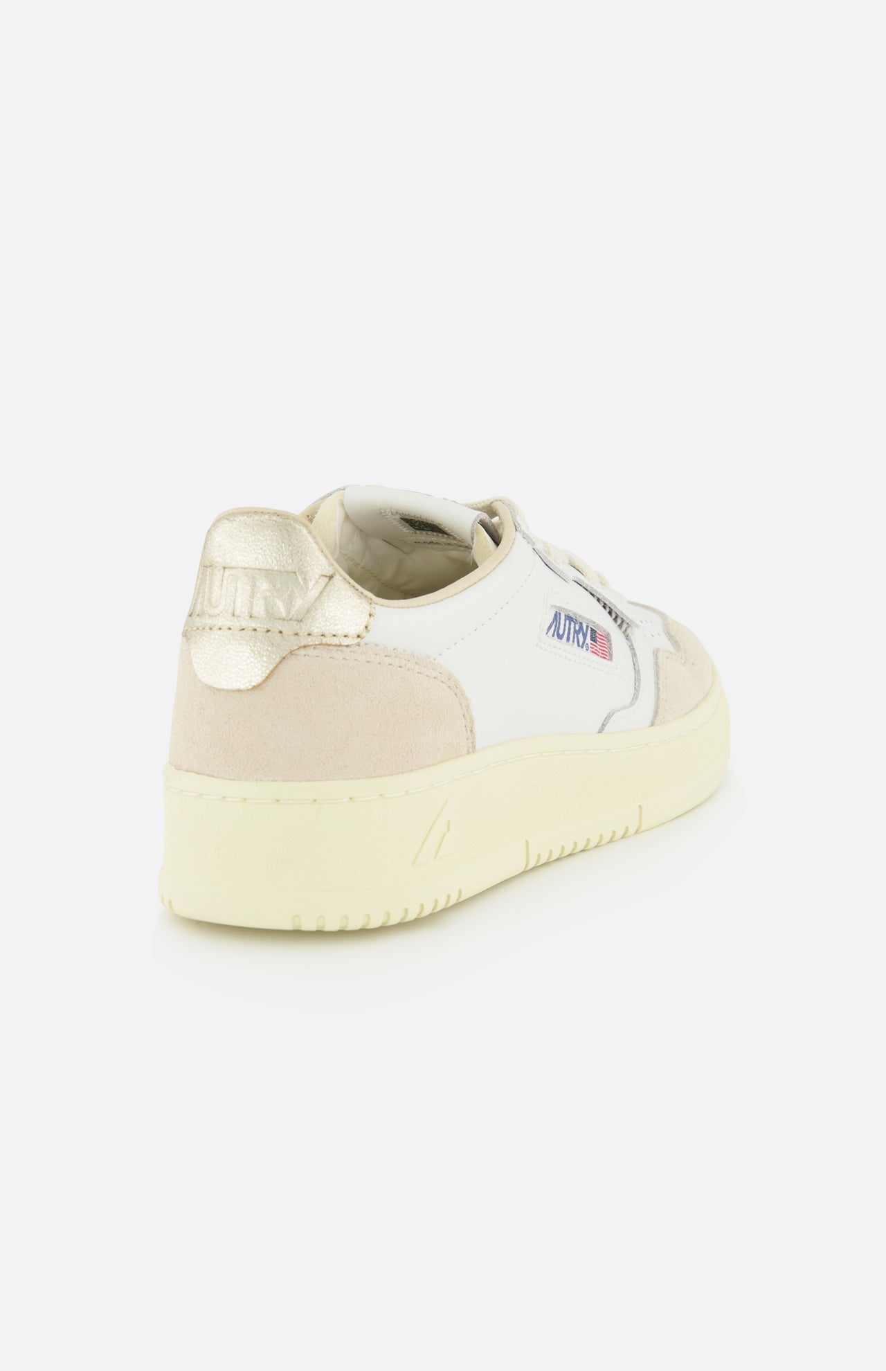Introducing the Medalist Low Gold Heel Sneaker by AUTRY—a white leather sneaker enhanced with a beige accent, distinctive gold heel, and cream platform sole. Seen from a back side angle, it proudly features AUTRY branding on both the heel and side, offering an elevated take on iconic 1980s tennis shoe style.