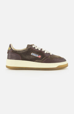 Introducing the AUTRY Medalist Low Suede Sneaker with Croco-effect: a low-top sneaker crafted from rich dark chocolate brown suede with distinctive croco-effect detailing. It features crisp white laces, a gum sole, and is finished with a small American flag logo on the side that reads AUTRY. Inspired by classic 1980s tennis shoes, this design effortlessly blends vintage appeal with contemporary style.