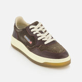 The AUTRY Medalist Low Suede Sneaker with Croco-effect is shown on a white background, featuring brown and olive tones, white laces, a beige sole, and a small American flag patch on the side. Its dark chocolate brown suede accents evoke the style of classic 1980s tennis shoes.