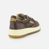 Introducing the AUTRY Medalist Low Suede Sneaker with Croco-effect: a brown low-top crafted from dark chocolate suede, boasting a refined crocodile-effect texture. This sneaker is highlighted by AUTRY’s signature yellow branding on the heel, a crisp white sole, and a tan gum outsole—capturing the authentic vintage style of 1980s tennis shoes when seen from the back angle.