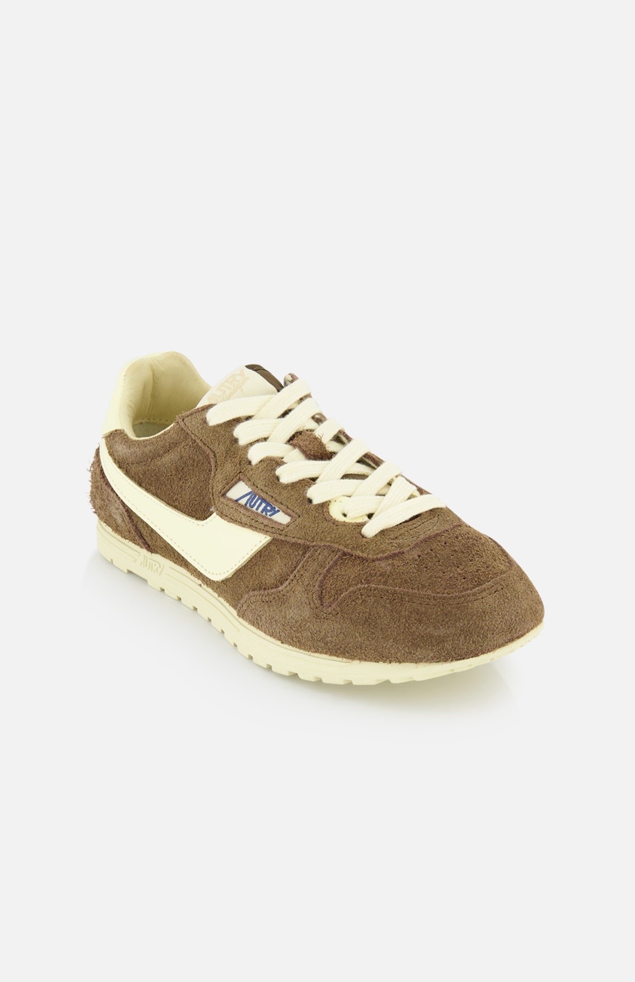 The Autry Windspin Low Brushed Suede Sneaker features a brown and cream 60s-inspired design with a textured suede upper, cream laces and sole, plus a blue and white logo tag on the side, shown against a white background.