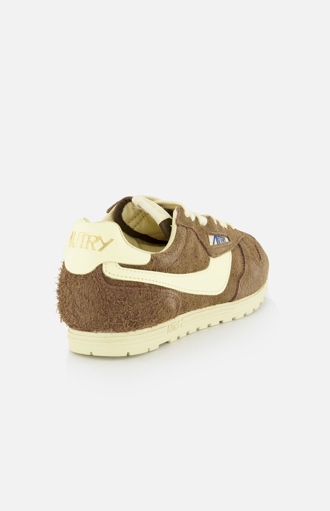 The Autry Windspin Low Brushed Suede Sneaker features dark brown suede, cream accents and sole, and branded heel, shown from the back left against a white background—evoking vintage sneaker charm.